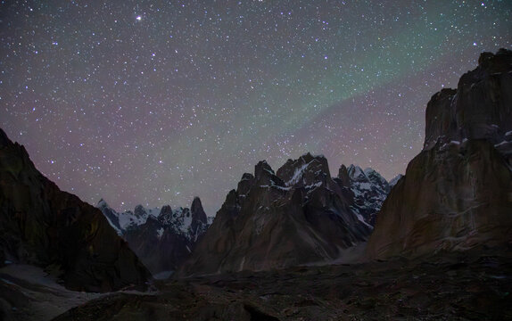 View of Trango Towers in the Karakoram mountain range under a starry night sky with faint aurora borealis in Ghakhar, Punjab, Pakistan.
