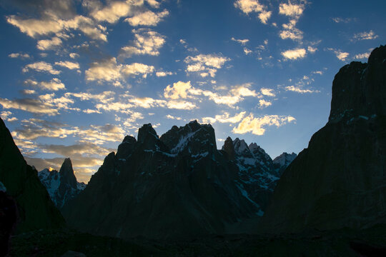 View of Trango Towers mountain range under a dramatic sunset sky with scattered clouds in Gilgit-Baltistan, Pakistan.
