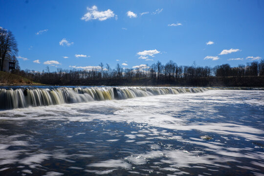 View of Ventas Rumba, the widest waterfall in Europe, with flowing water cascading over the limestone ledge under a clear blue sky in Kuldiga, Kuldigas novads, Latvia.