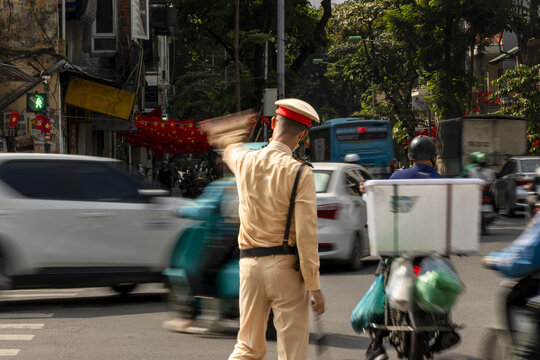 View of a traffic police officer in uniform directing the flow of vehicles and scooters on a busy street in Hanoi, Ha Noi, Vietnam.