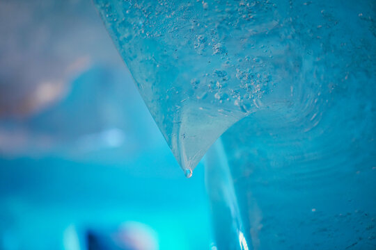 View of melting ice formations with a single water droplet hanging from a sharp edge of the Rhone Glacier in Obergoms, Valais, Switzerland.