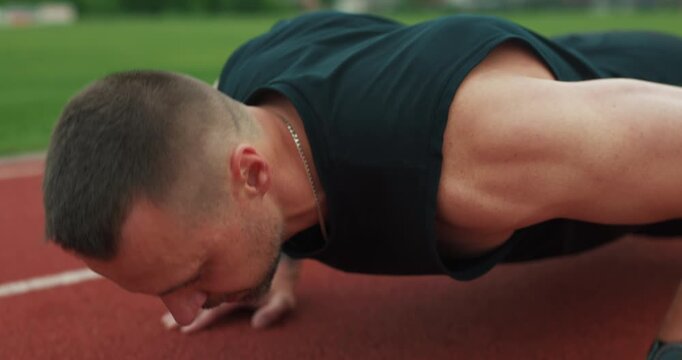 Strong muscular sportsman exercising push-ups during stadium workout