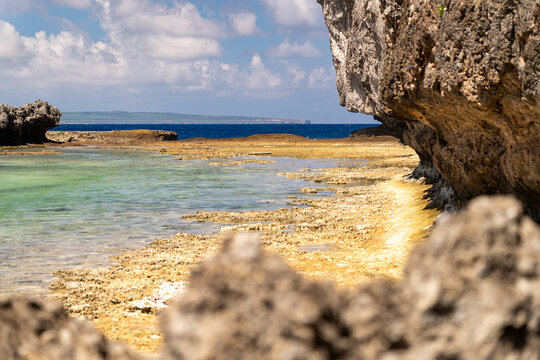 View of the rocky coastline and turquoise waters of Chigit Beach with limestone cliffs and a clear blue sky in Northern Tinian, Tinian, Northern Mariana Islands.