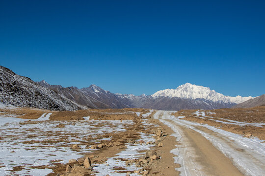 View of the snow-capped Nanga Parbat peak rising above the vast, partially snow-covered Deosai plains with a dirt road leading through the landscape in Astore, Gilgit, Pakistan.