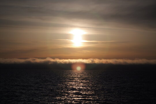 View of the sun setting over the Baltic Sea with a low bank of clouds and shimmering water in Liepaja, Latvia.
