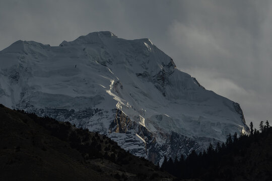 View of the snow-capped peak of Rakaposhi mountain with glacial ice and rocky slopes under dramatic light in Hunza Nagar, Gilgit, Pakistan.