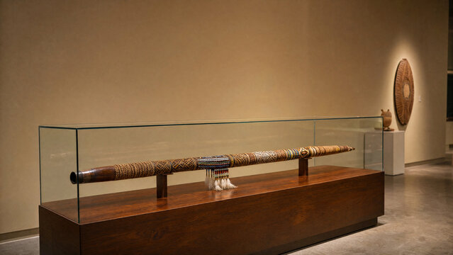 An ornate ceremonial blowpipe displayed in a museum case.