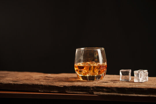 Whiskey Glass with Ice Cubes on Wooden Surface Against Dark Background
