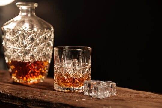 A glass liquor bottle and whiskey with ice on a wooden table.
