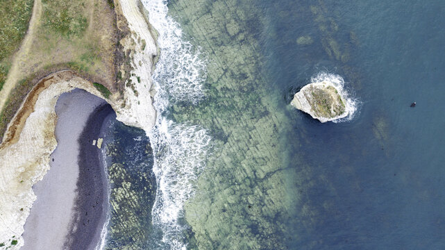 Aerial view of the white chalk cliffs and sea stack at Freshwater Bay with turquoise water and a pebble beach in Freshwater, Isle of Wight, United Kingdom.