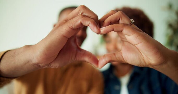Couple, kiss and hands with heart in house, commitment and love symbol with partner and anniversary. People, bonding and shape with gesture in living room, care and connection with spouse in home