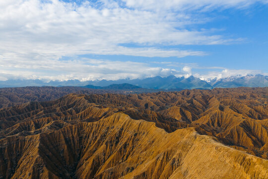 Aerial view of the rugged orange eroded hills and badlands of Ak Say Canyon under a blue sky with clouds in Ak Say, Issyk-Kul Region, Kyrgyzstan.