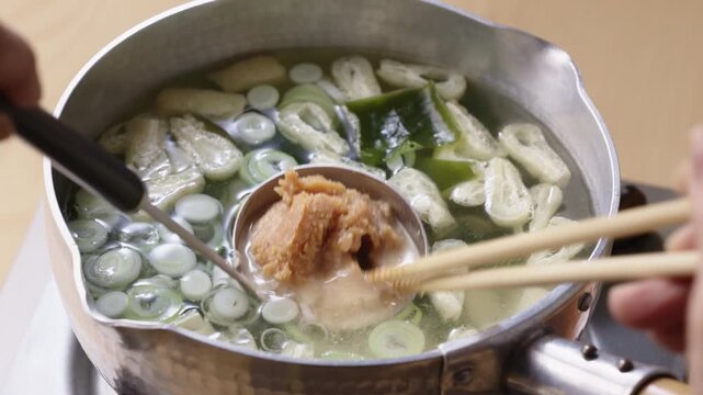 Dissolving miso paste into soup with a ladle and chopsticks in a pot