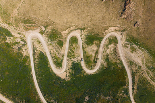 Aerial view of the winding switchbacks of 33 Parrots Pass with a car driving on the dirt road through the green mountains in Jety - Oguz, Issyk-Kul Region, Kyrgyzstan.