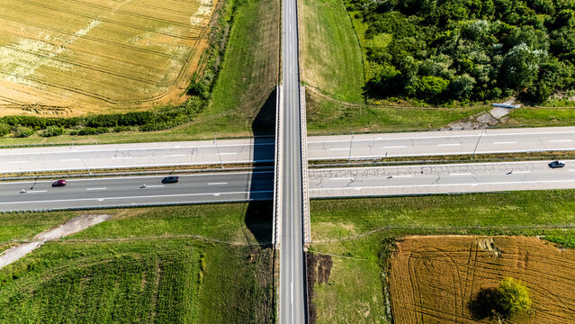 Aerial view of a highway overpass bridge crossing a multi-lane motorway with cars driving through green agricultural fields in Sremska Mitrovica, Serbia.