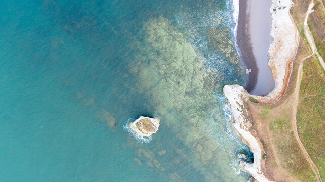 Aerial view of Freshwater Bay featuring turquoise water, white chalk cliffs, a small sea stack, and a pebble beach in Freshwater, Isle of Wight, United Kingdom.
