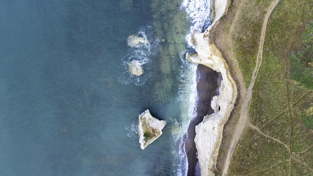 Aerial view of the white chalk cliffs and turquoise waters of Freshwater Bay with sea stacks and coastal paths in Freshwater, Isle of Wight, United Kingdom.