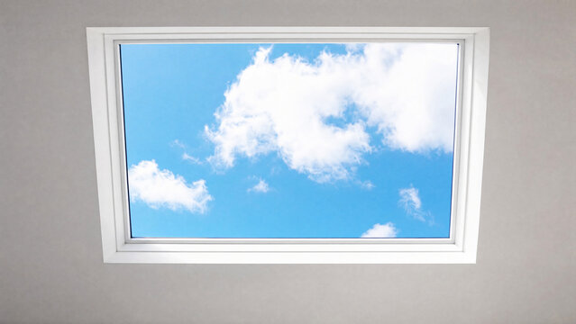 Rectangular sunroof framing moving clouds against a blue sky, minimalist architectural detail.