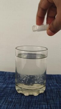 Closeup of hand putting cocaine, morphine or heroin narcotic white drug powder inside glass of water or alcohol drink. Consuming narcotic substance concept.