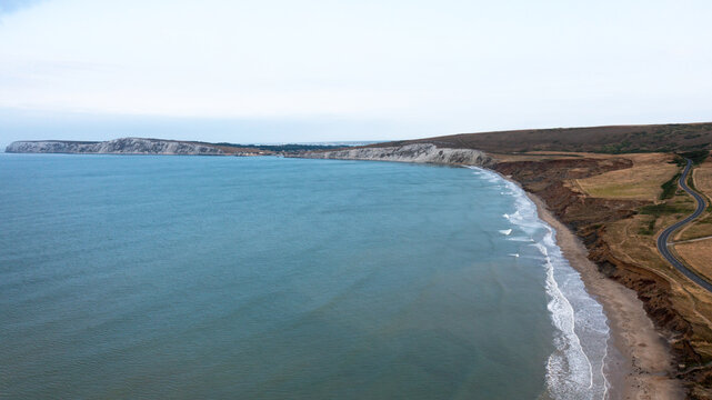Aerial view of Compton Bay featuring the sandy beach, rugged cliffs, and a winding coastal road in Newport, Isle of Wight, United Kingdom.
