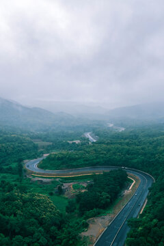 Aerial view of a winding highway cutting through lush tropical forest and mountain landscape under misty skies. Ideal for ESG reports, sustainability strategies, green finance presentations, climate r