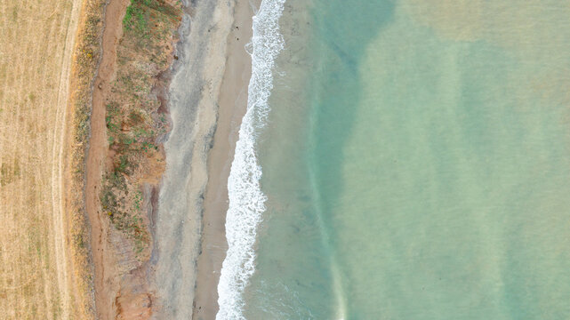 Aerial view of Compton Bay with turquoise waves washing onto the sandy shore and rugged cliffs in Newport, Isle of Wight, United Kingdom.