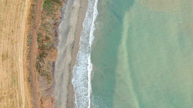 Aerial view of the sandy shoreline at Compton Bay with gentle waves washing over the sand and coastal cliffs in Newport, Isle of Wight, United Kingdom.