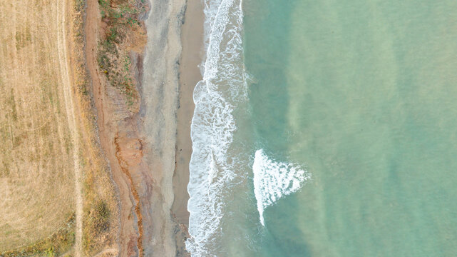 Aerial view of the sandy beach and turquoise water at Compton Bay with coastal cliffs and a dry field in Newport, Isle of Wight, United Kingdom.