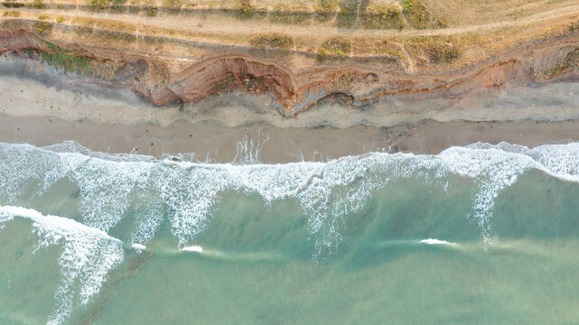 Aerial view of the reddish cliffs and sandy beach at Compton Bay with turquoise waves crashing on the shore in Newport, Isle of Wight, United Kingdom.