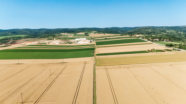 Aerial view of agricultural patchwork fields and rolling hills under a clear blue sky in Sremska Mitrovica, Serbia.