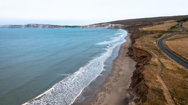 Aerial view of the sandy beach and white chalk cliffs at Compton Bay with a winding coastal road along the grassy hills in Newport, Isle of Wight, United Kingdom.