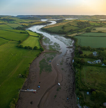 Aerial view of Frogmore Creek winding through lush green fields and rolling hills at low tide during golden hour in Kingsbridge, South Devon, United Kingdom.