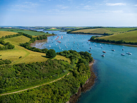 Aerial view of Salcombe Harbour with numerous sailboats moored in the blue estuary waters surrounded by rolling green hills and lush coastal landscape in Salcombe, Devon, United Kingdom.