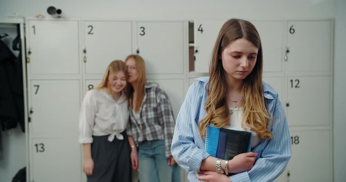 Teenage girl feeling excluded while classmates talk near lockers
