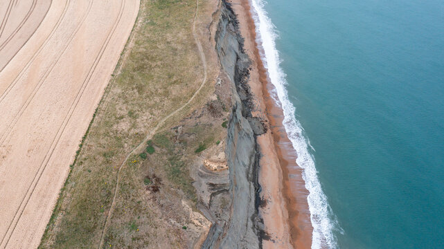 Aerial view of the dramatic cliffs at Whale Chine overlooking the turquoise sea and sandy beach with agricultural fields Ventnor, Isle of Wight, United Kingdom.