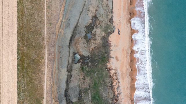 Aerial view of the eroded cliffs at Whale Chine with a coastal path and waves crashing on the sandy beach in Ventnor, Isle of Wight, United Kingdom.