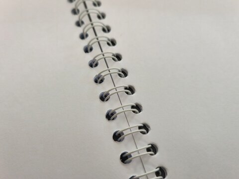 Close up of white spiral wire binding on a blank open notebook, macro view of metal twin loop wire ring binder on clean paper page, school stationery or corporate office diary concept