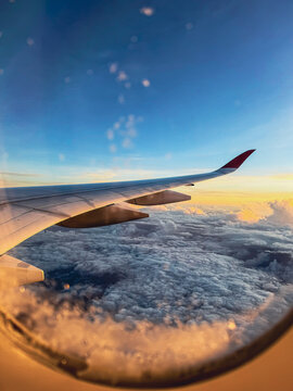 Aerial view of an airplane wing soaring above a dense blanket of clouds at sunset with golden light hitting the horizon in Africa.