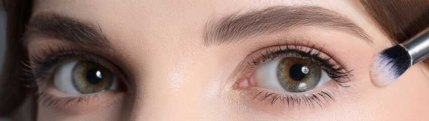 Naklejka premium Applying nude eye shadow with makeup brush onto woman's face, closeup