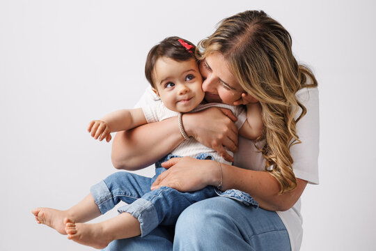 Woman in light clothes have fun with cute child baby girl. Mother, little kid daughter isolated on pastel white wall background, studio portrait. Mother's Day