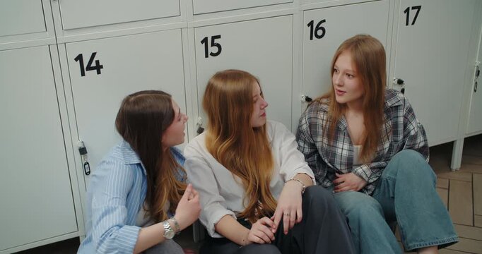 Three teenage friends talking while sitting by school lockers