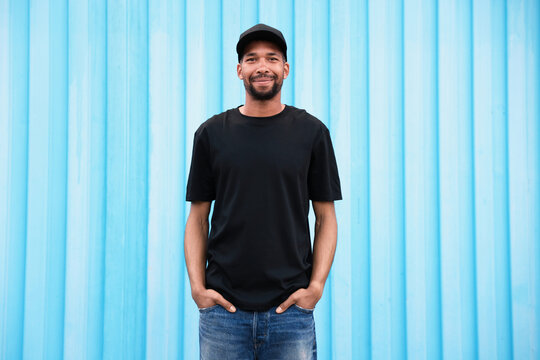 Happy African-American man wearing stylish outfit near light blue wall outdoors