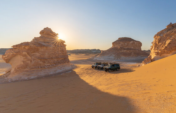 View of off-road vehicles parked near unique chalk rock formations in the White Desert at sunset, Egypt.
