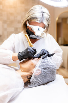 Beautician applying permanent makeup to woman's eyelid