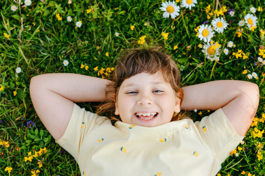 Happy child girl resting in flower meadow with hands behind head