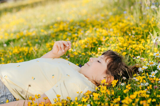 Child relaxing on flowering meadow surrounded by yellow wildflowers