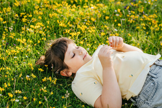 Child girl lying in wildflower meadow and looking at blossom