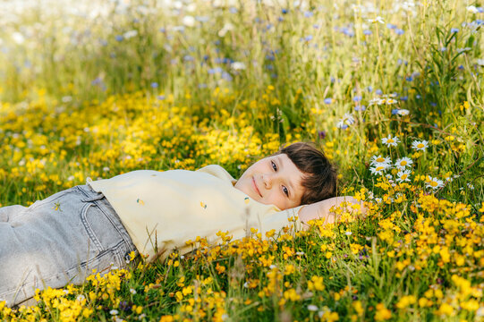 Child girl lying in flowering meadow surrounded by yellow blooms
