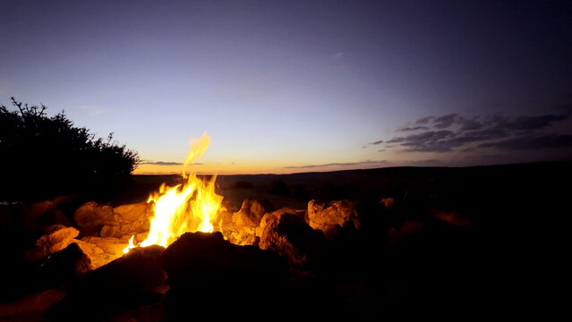 View of a campfire burning brightly among rocks at dusk in Kruger National Park, Skukuza, Mpumalanga, South Africa.