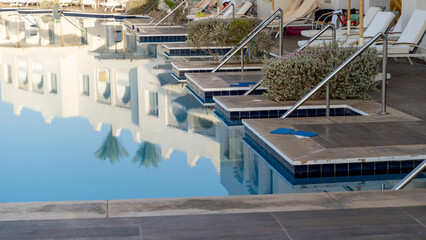 Fototapeta premium Crystal-clear pool reflects white buildings and palm trees